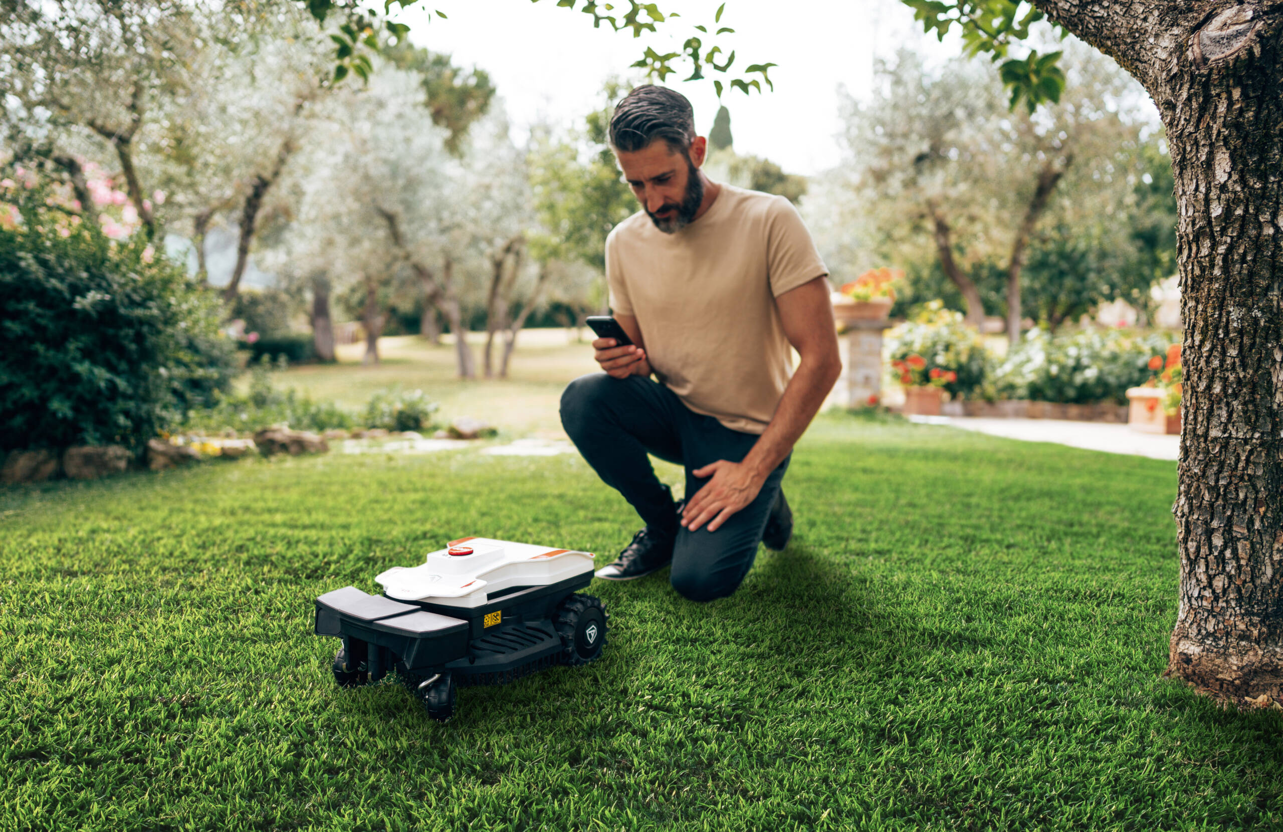 Mężczyzna obsługuje robota koszącego przez telefon na zielonej trawie